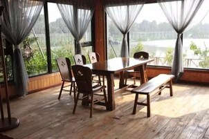 A wooden dining table with chairs, a bench, and a view of a body of water through large windows with sheer curtains.