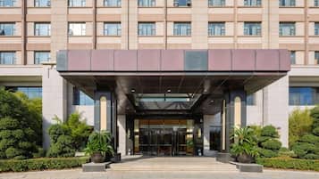 Un hotel de varios pisos con un vestíbulo cubierto, amplias ventanas y un acceso ajardinado.