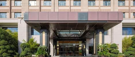 A multi-story hotel with a covered entrance, large windows, and a landscaped entrance area.
