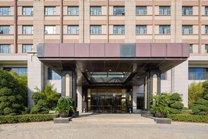 Un hotel de varios pisos con un vestíbulo cubierto, amplias ventanas y un acceso ajardinado.