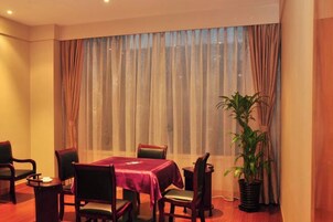 Un comedor con una mesa dispuesta para cuatro personas, rodeada de sillas, una planta en maceta y un amplio ventanal con cortinas.