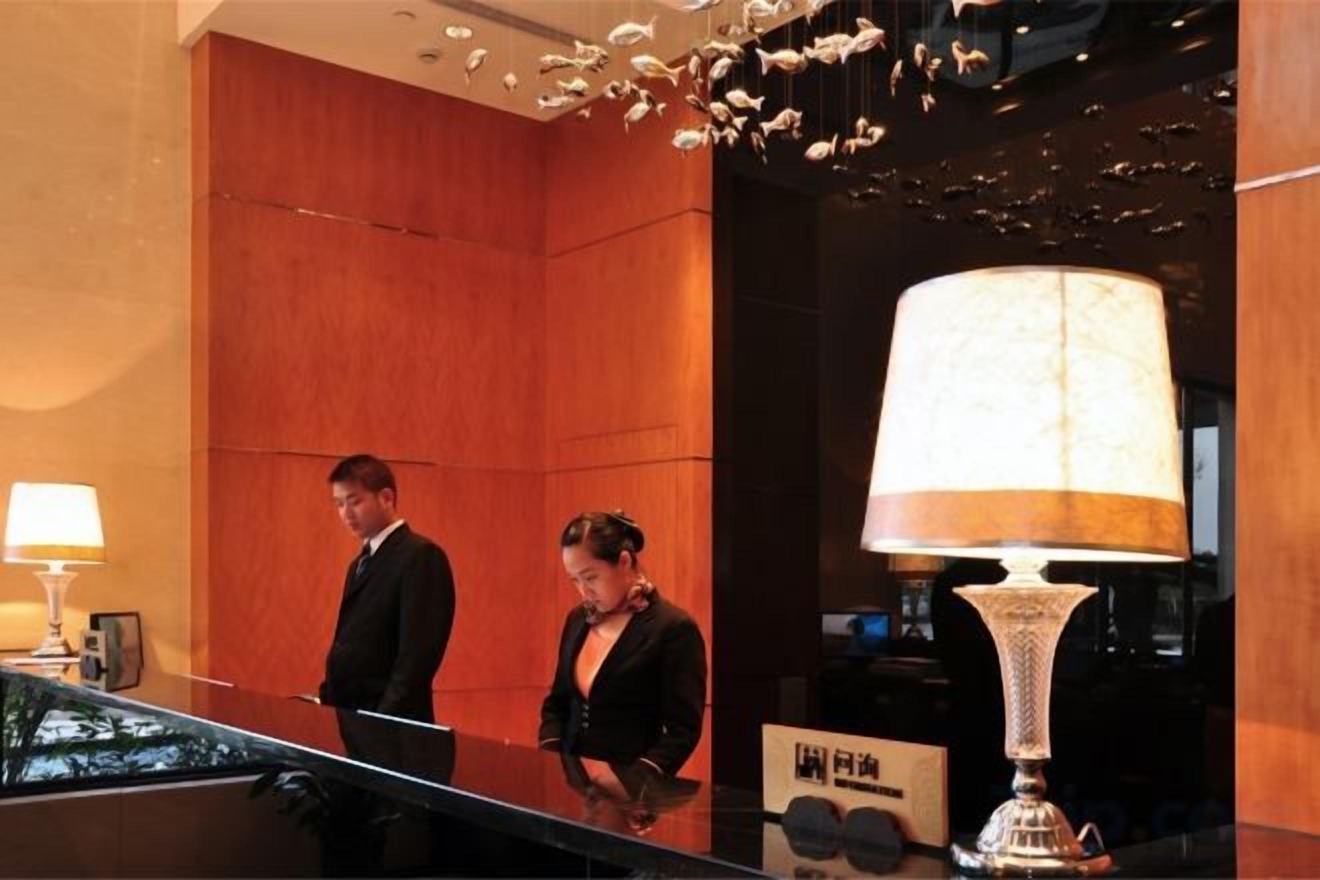 Un espace d’accueil avec un comptoir de réception, un homme et une femme debout, et une grande lampe.