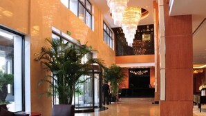 A spacious lobby with a high ceiling, large windows, and a central plant area. - Oriental Hotel (Taicang)