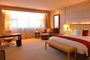 A hotel room with a bed, desk, chair, and a large window. - Oriental Hotel (Taicang)