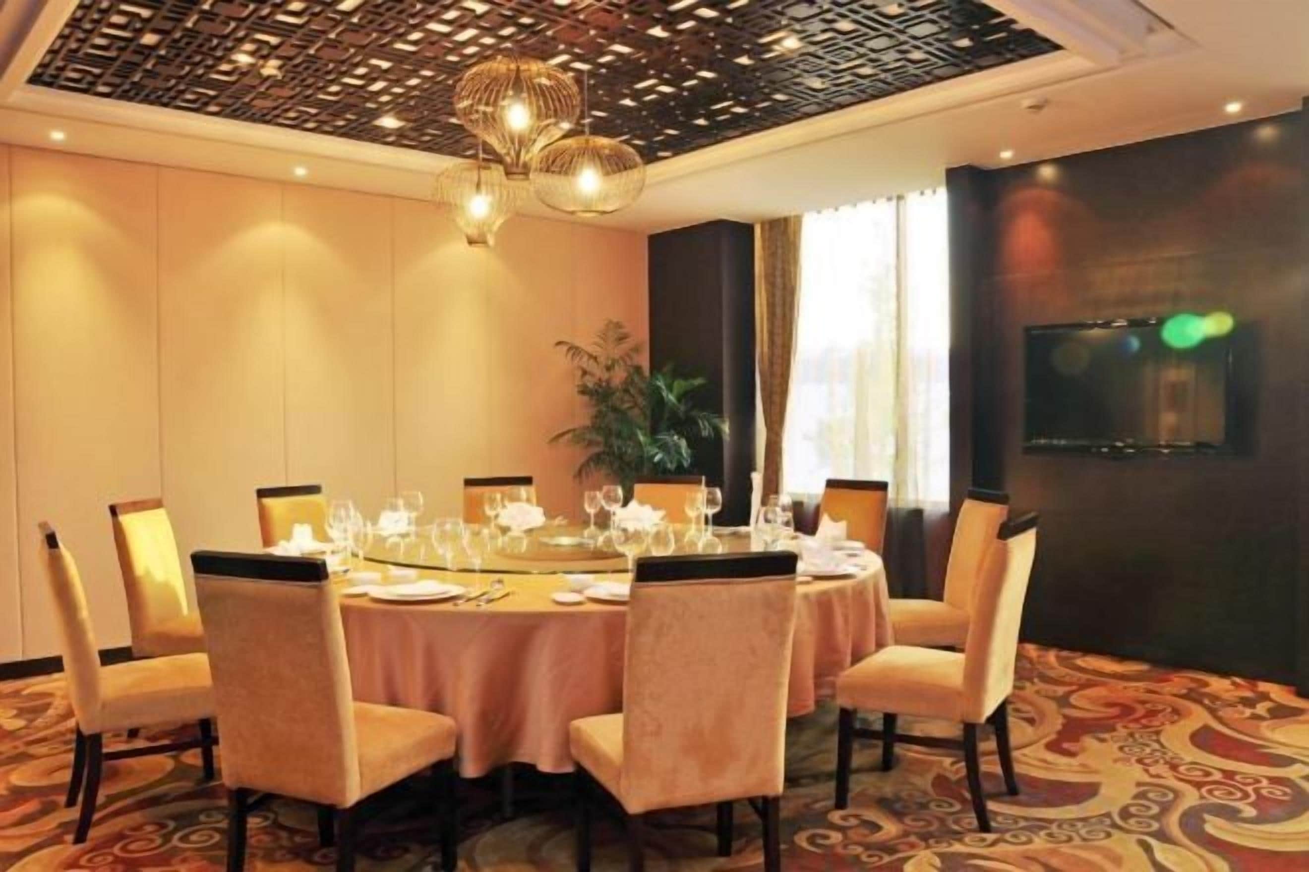A dining area with a round table set for six, surrounded by chairs, in a room with patterned carpet and a decorative ceiling.