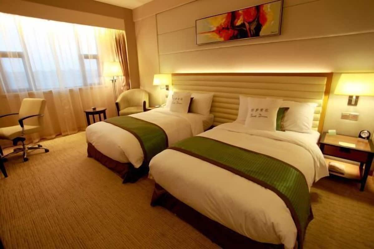 A hotel room with two beds, a chair, a desk, and a painting on the wall.