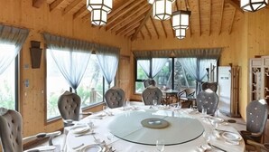 A wooden dining room with a round table set for six, large windows, and a high ceiling with exposed beams. - Oriental Hotel (Taicang)