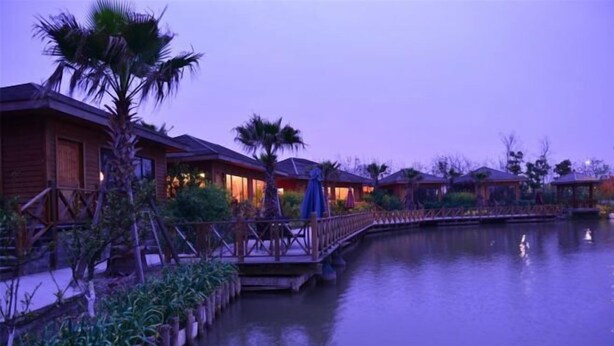 A series of wooden cabins with a water body in the foreground, connected by a wooden bridge. - Oriental Hotel (Taicang)