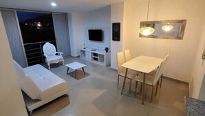 Ein modernes Wohnzimmer mit Flachbildfernseher, Esstisch mit Stühlen, einer Couch und einem kleinen Couchtisch.