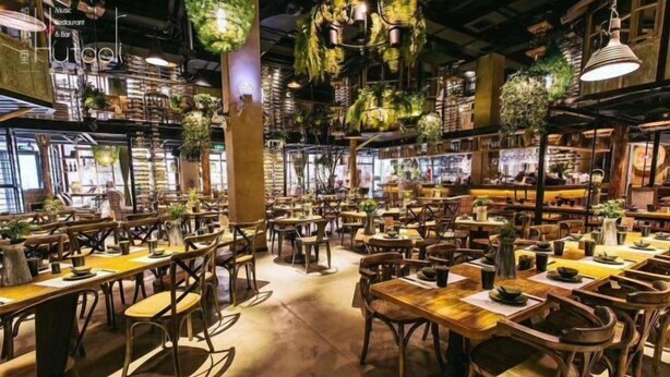 A restaurant interior with multiple dining tables and chairs, wooden floors, and hanging plants. - Huaijia Art Hotel (Qinzhou)
