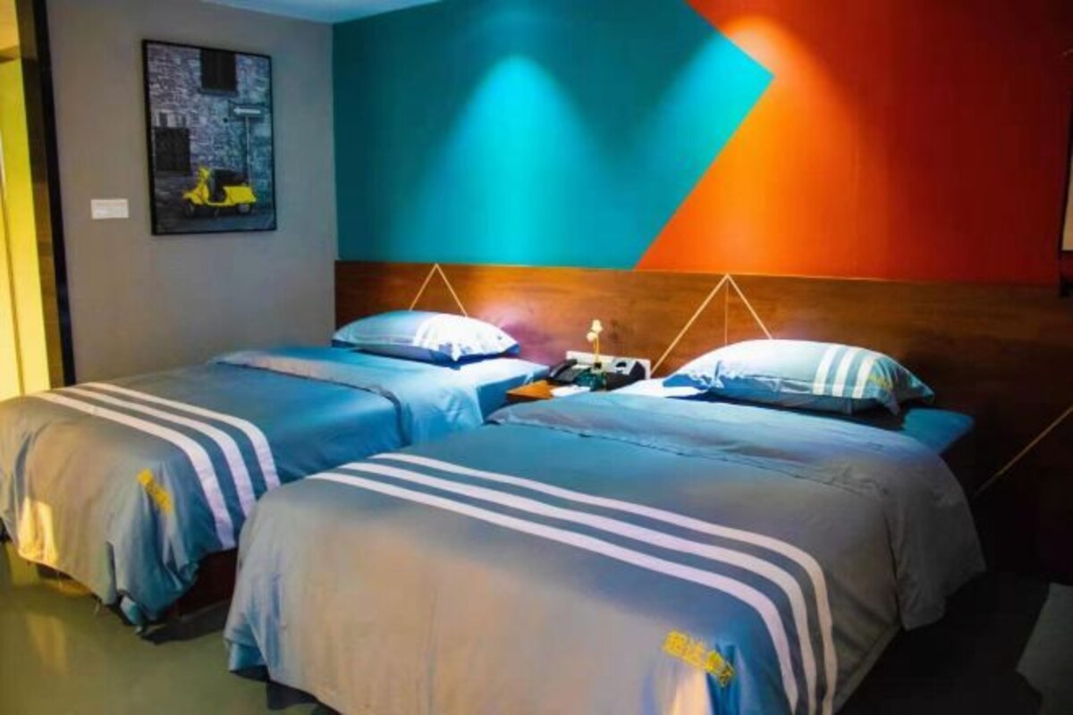 Una habitación de hotel con dos camas, cabecero de madera y pared colorida.