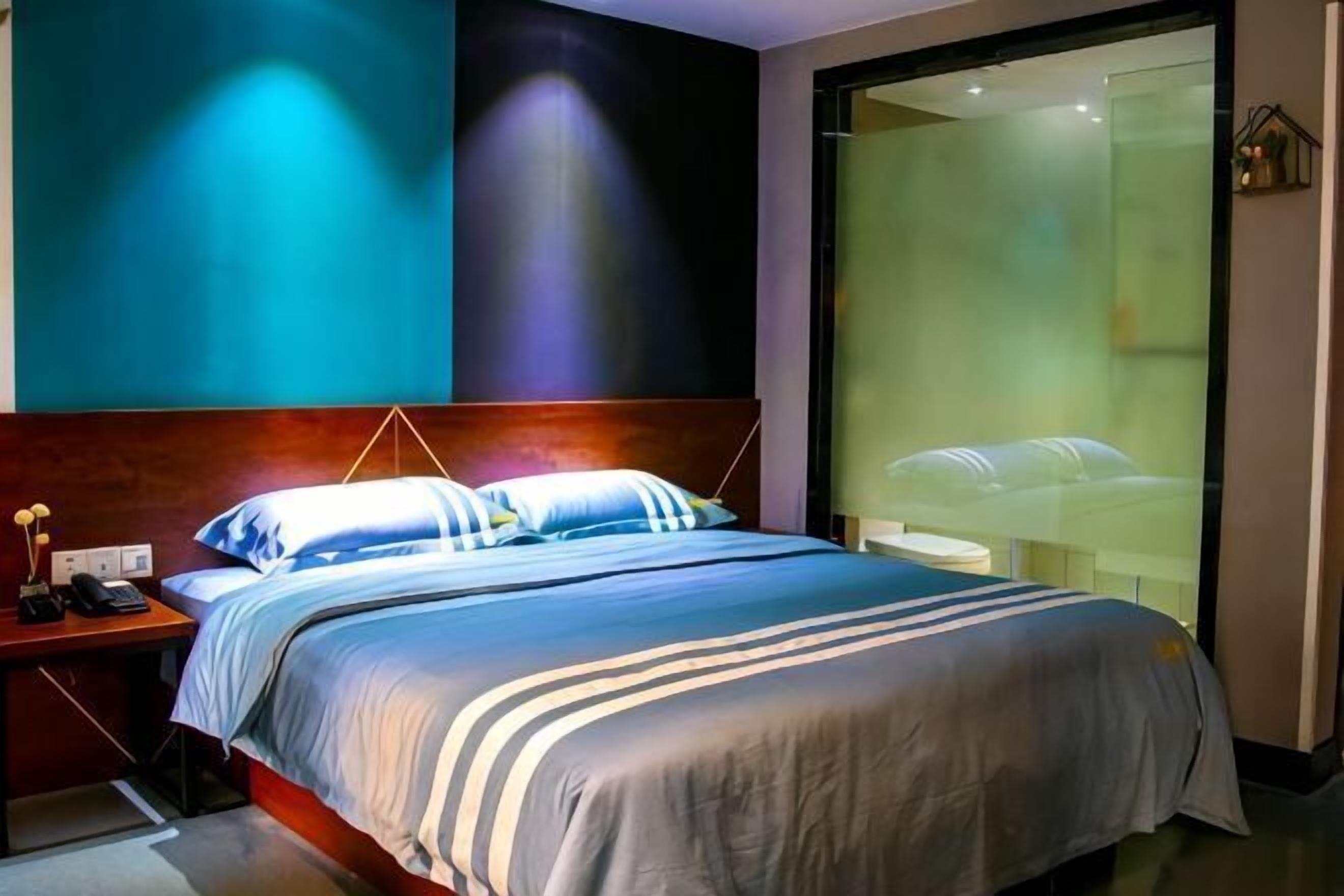 Ett modernt hotellrum med en stor säng, ett nattduksbord och en vägg av glas som avgränsar rummet.