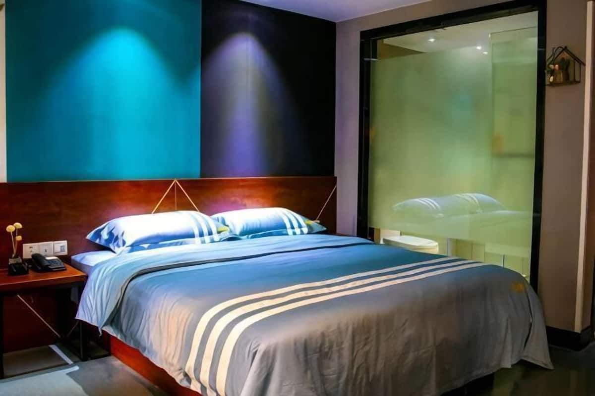 Una habitación de hotel moderna con una cama grande, una mesita de noche y una pared divisoria de vidrio.
