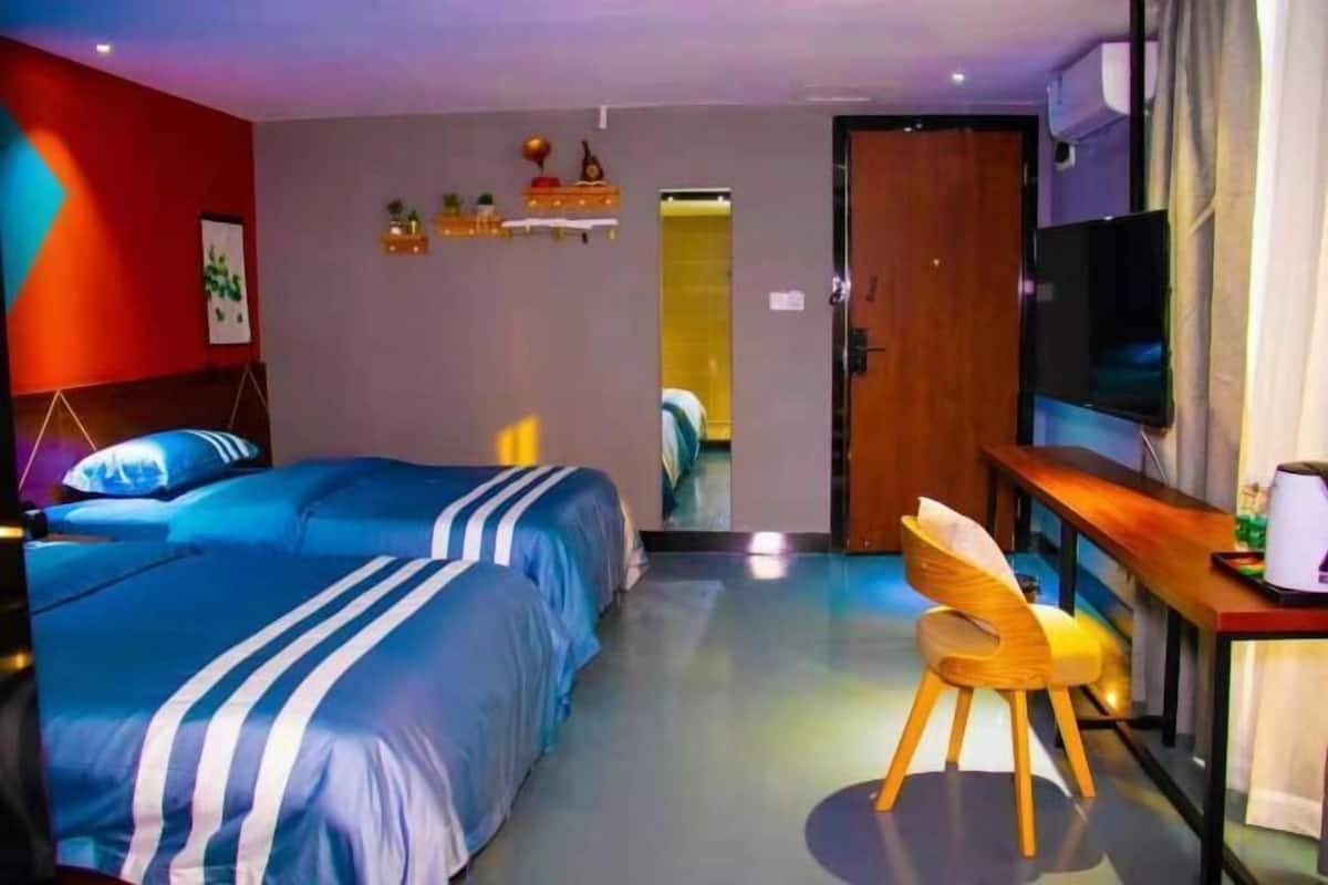 Habitación de hotel con dos camas, un escritorio, una silla, un televisor y una puerta que da a otra habitación.