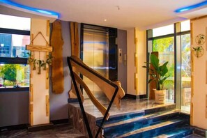 Un vestíbulo de hotel con una escalera de mármol, un mostrador de recepción y un ventanal con vistas al exterior.