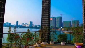A balcony with potted plants, a brick pillar, and a view of a city skyline across a body of water. - Huaijia Art Hotel (Qinzhou)