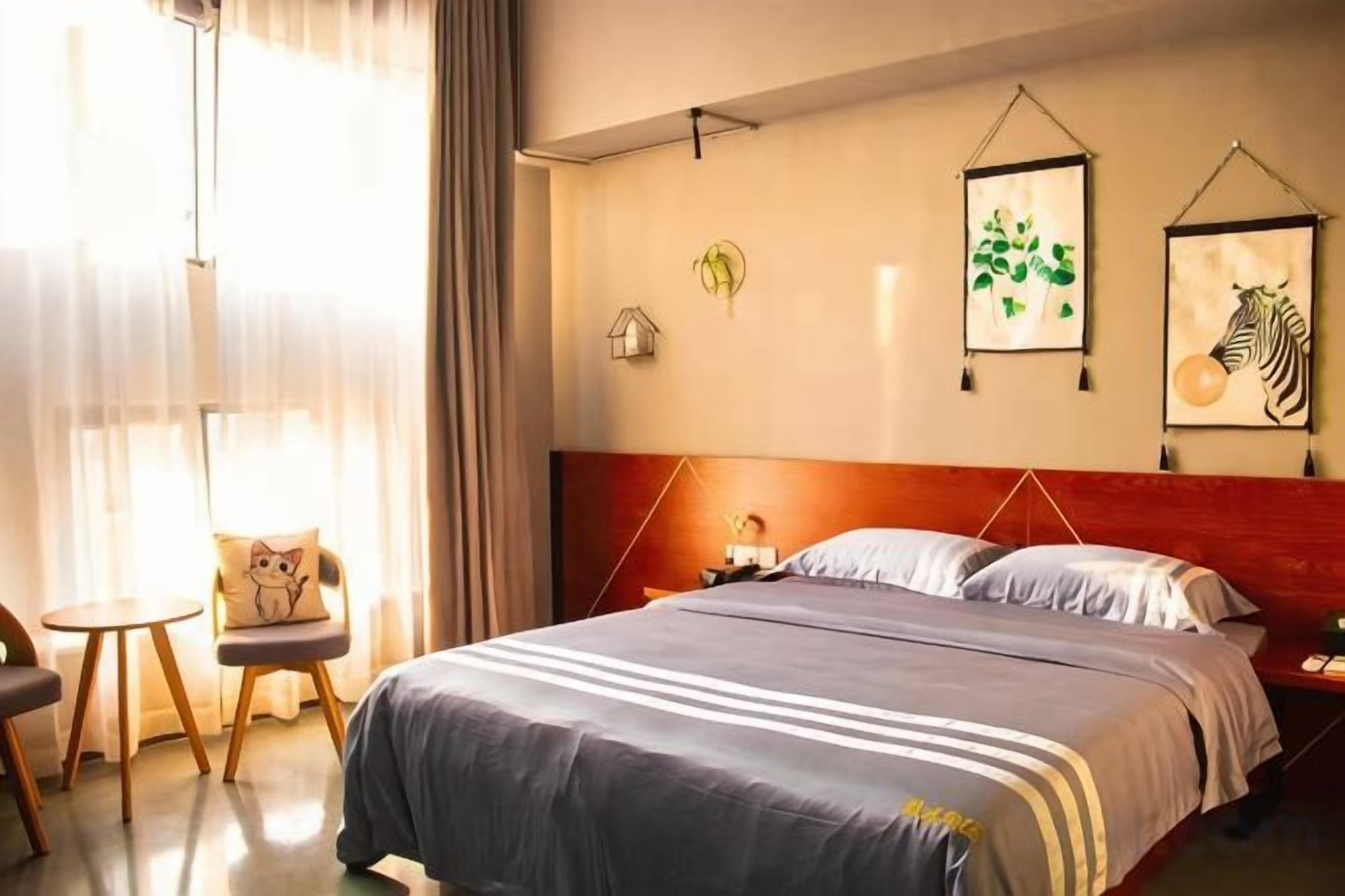 A hotel room with a bed, bedside table, chair, and artwork on the wall.