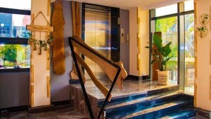 A modern hotel lobby with a marble staircase, a glass elevator, and a large potted plant. - Huaijia Art Hotel (Qinzhou)