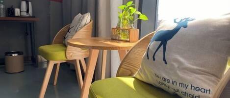 Un coin salon accueillant avec un fauteuil confortable aux coussins verts, une table en bois ornée d’une plante et un coussin décoré de la silhouette d’un cerf.