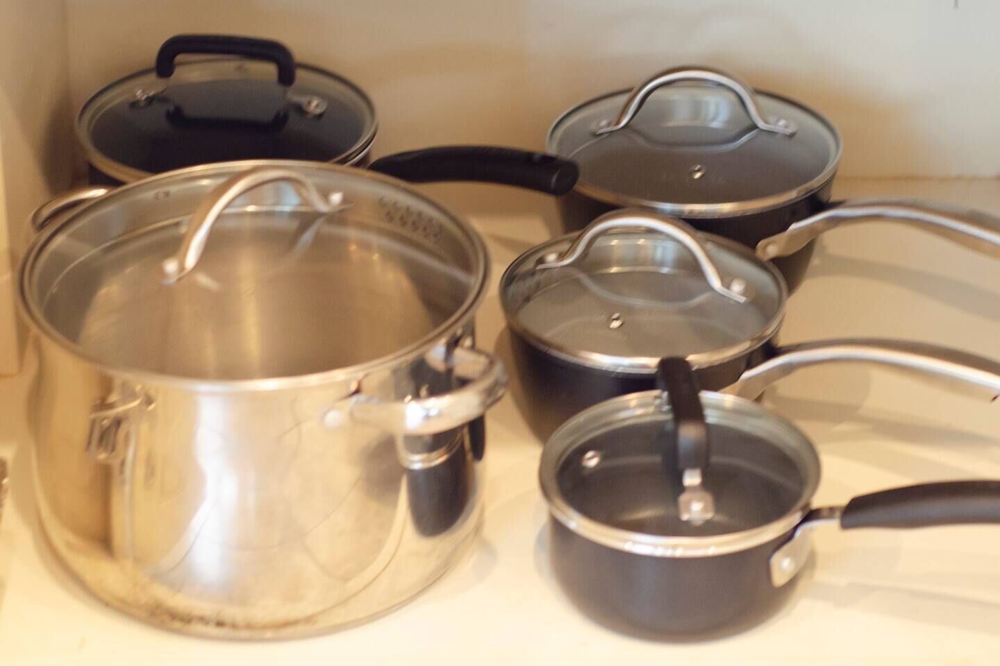 A kitchen with stainless steel pots and pans, some with lids and handles.