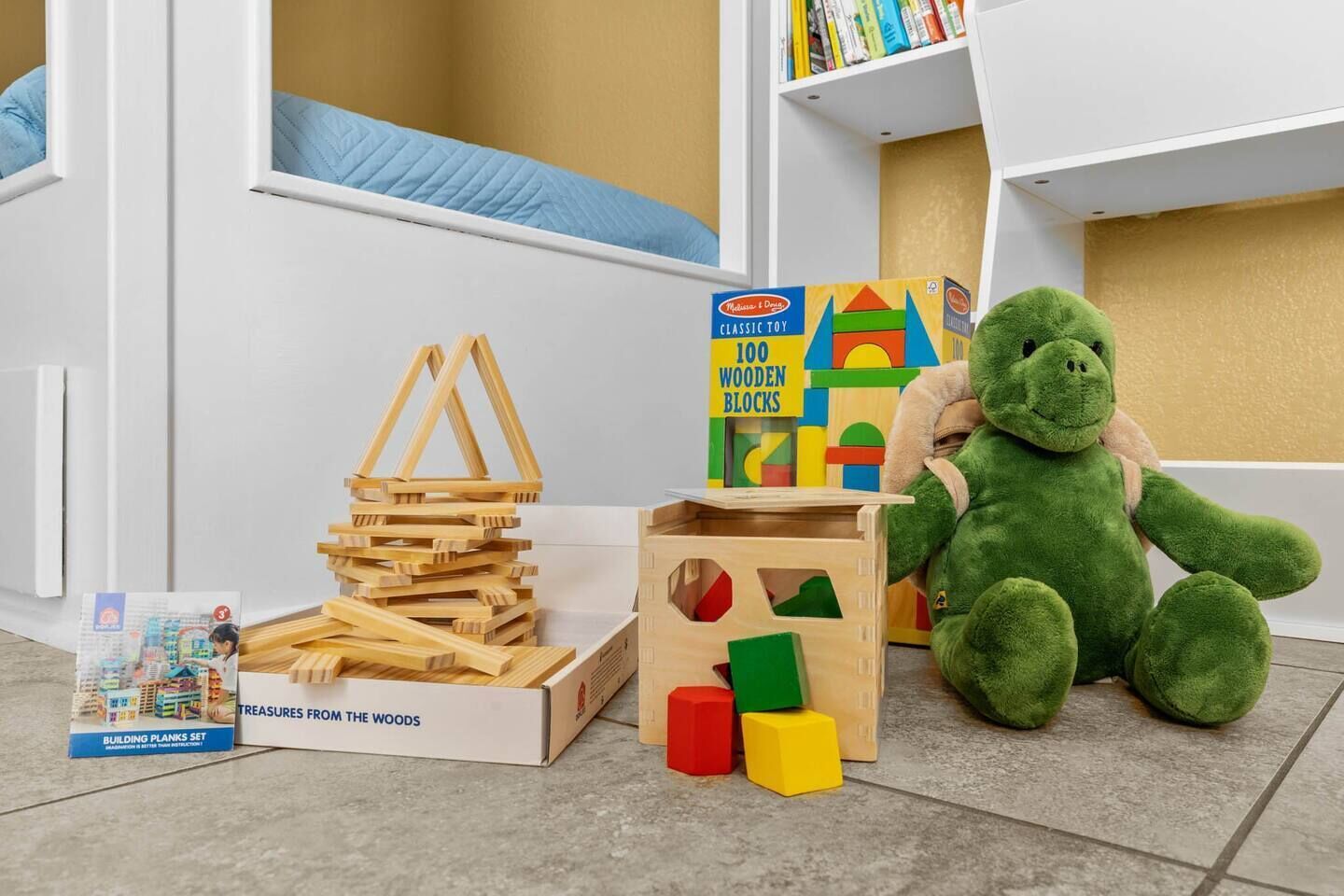 Ein Kinderspielbereich mit Holzbausteinen, einem Bauklotzset und einem grünen Stofftier.