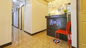 Zona de recepción de hotel con un mostrador, una silla roja y un indicador en el suelo que marca el distanciamiento social.
