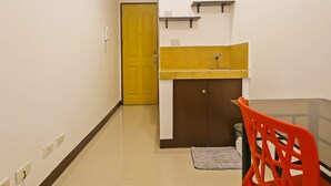 Un pasillo estrecho con una puerta amarilla, una kitchenette pequeña con un lavamanos amarillo y una mesa con una silla naranja.