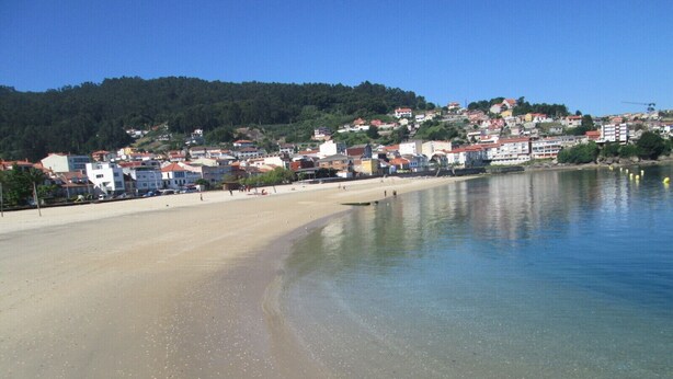 A beach with clear water, a sandy shore, and buildings in the background.