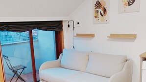 A modern living room with a sofa, a small table, and a sliding glass door leading to a balcony with a chair.