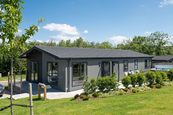 A modern house with a grey exterior, large windows, and a well-maintained garden. - Juniper Lodge, 28 Roadford Lake Lodges (Lifton)