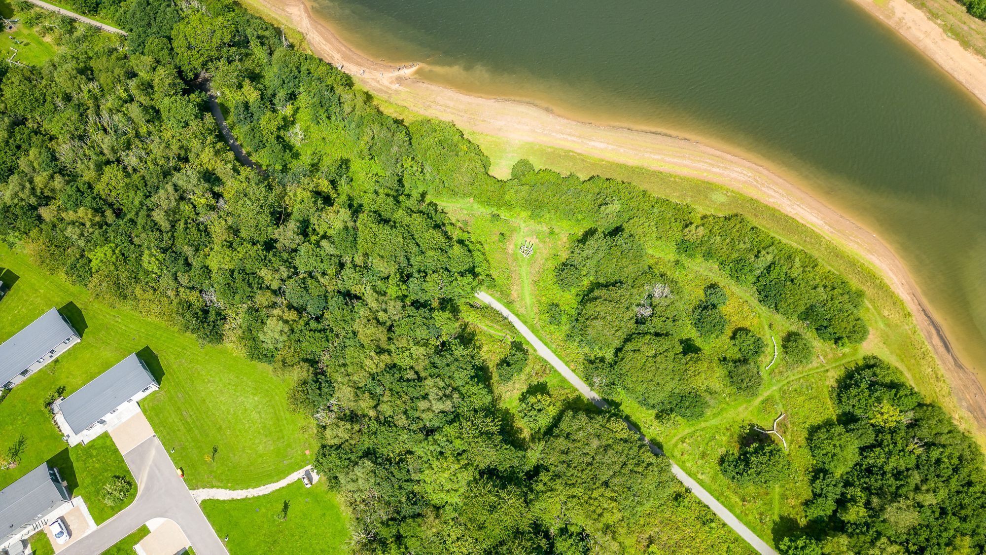 Vista aerea di una zona residenziale con un grande parco verde, una spiaggia e una strada.