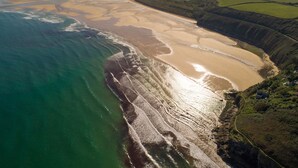 An aerial view of a coastal area with a sandy beach, a river, and surrounding green fields.
