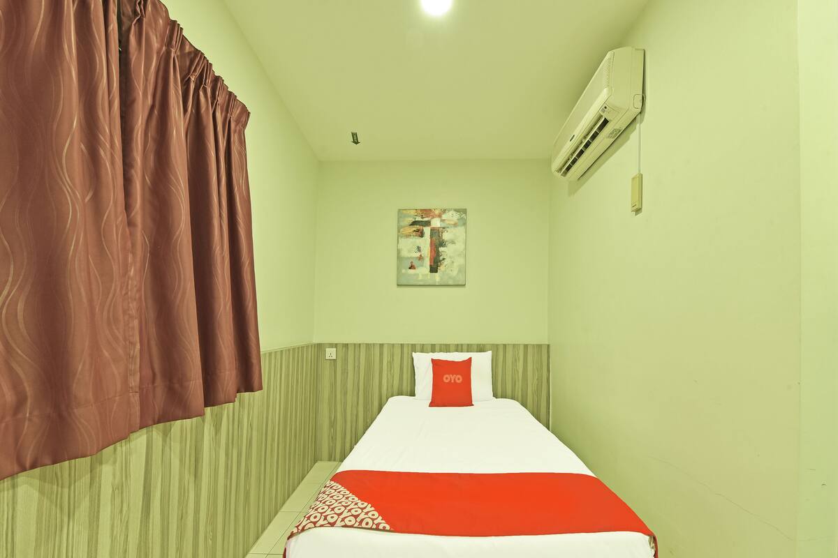 Una cama individual con una colcha roja y blanca, un almohadón rojo y un aire acondicionado de pared.