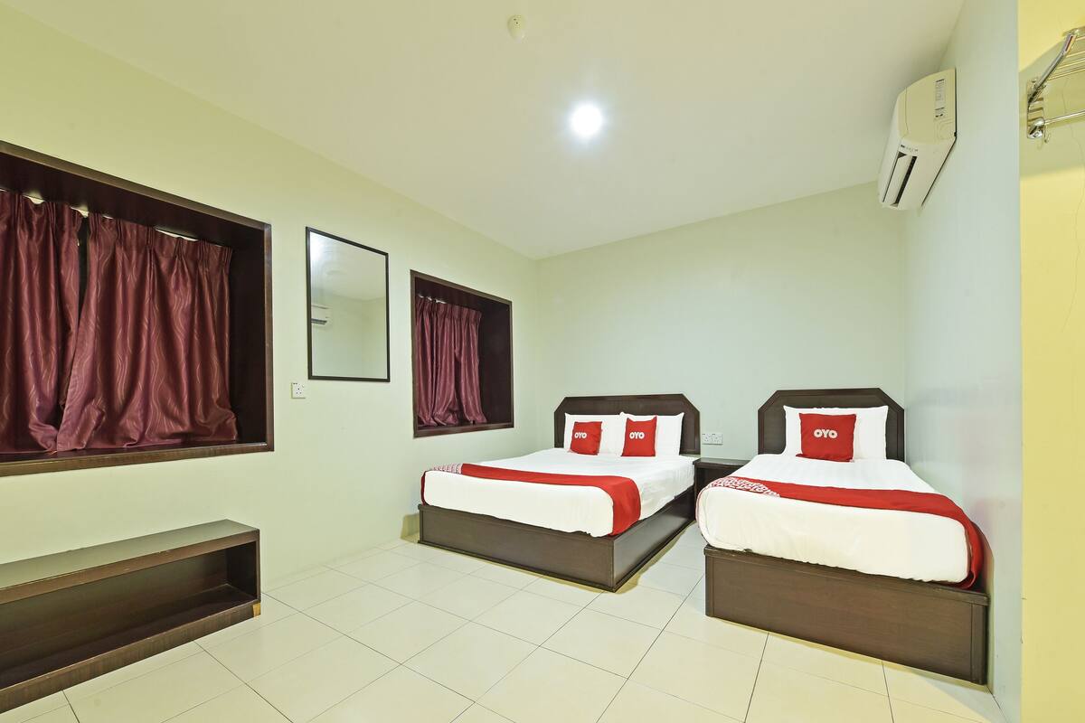 Habitación de hotel con dos camas, un pequeño banco, un espejo y un equipo de aire acondicionado.