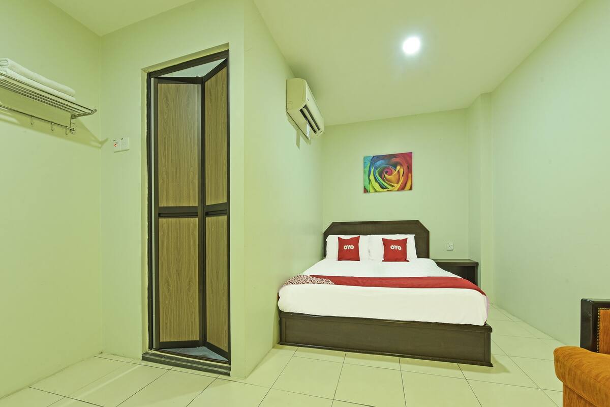 Habitación de hotel con cama, armario, aire acondicionado, una obra de arte colorida en la pared y una silla.