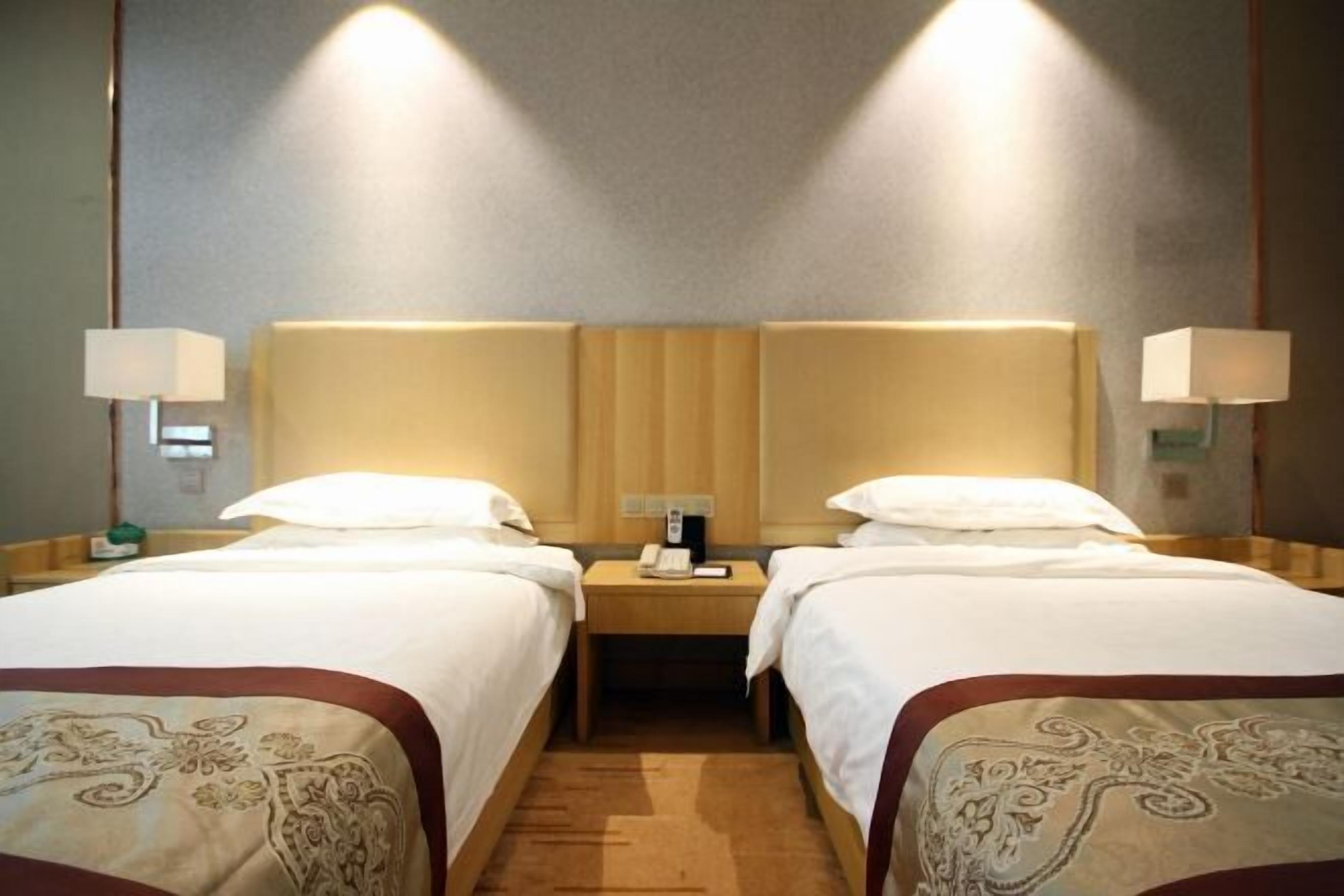 A hotel room with two beds, a nightstand with a phone, and wall-mounted lamps.