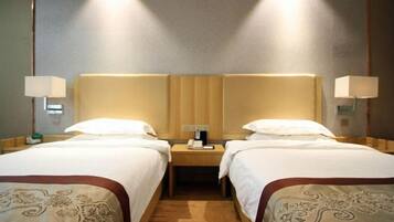 A hotel room with two beds, a nightstand with a phone, and wall-mounted lamps.