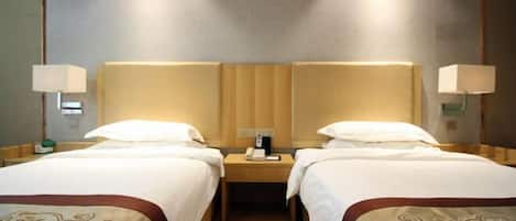 A hotel room with two beds, a nightstand with a phone, and wall-mounted lamps.