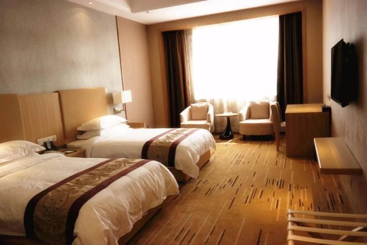 A hotel room with two beds, a desk, a chair, and a TV.