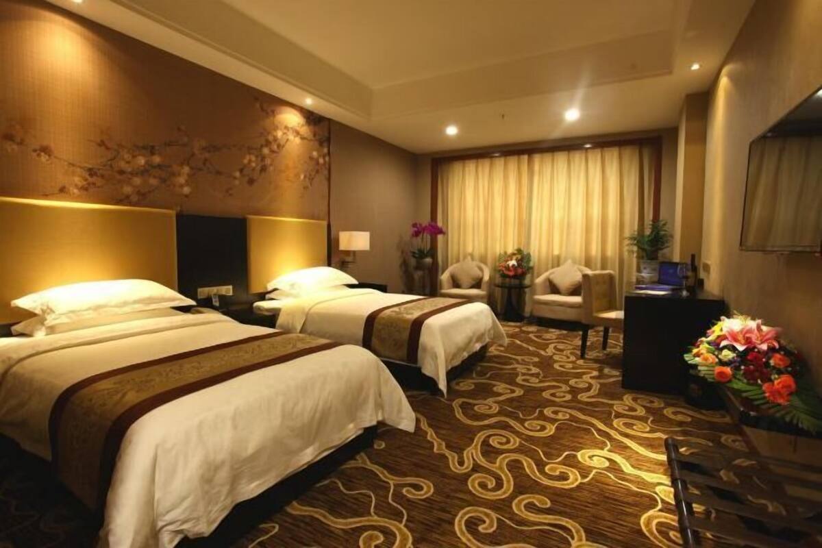 A hotel room with two beds, a sofa, a small table, a decorative wall, and a curtain.