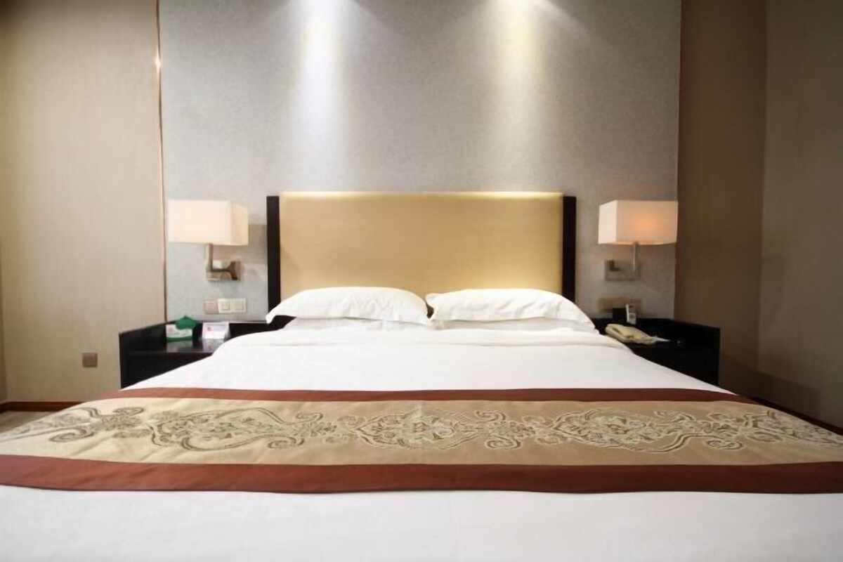 A hotel room with a large bed, two bedside tables with lamps, and a decorative bed runner.