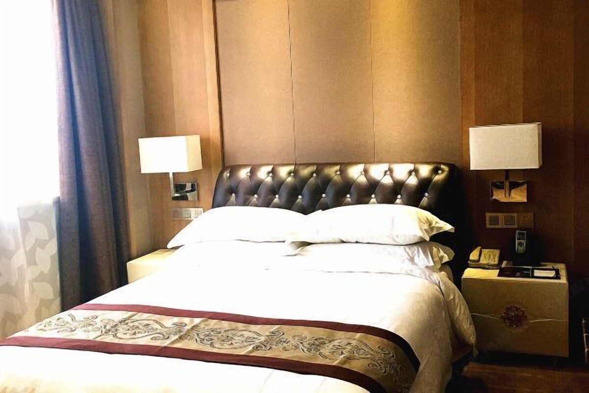 A hotel room with a large bed, two bedside lamps, a nightstand with a phone, and a wooden headboard.