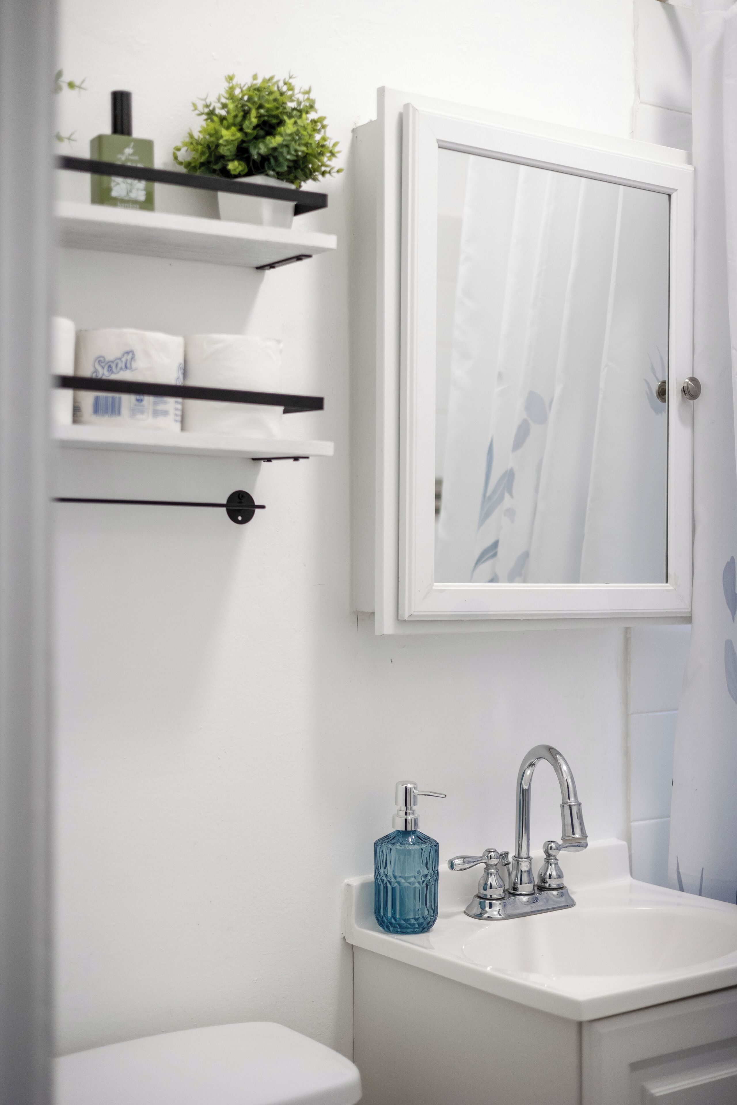 Une salle de bain avec un lavabo blanc, un miroir et des étagères contenant des articles de toilette.