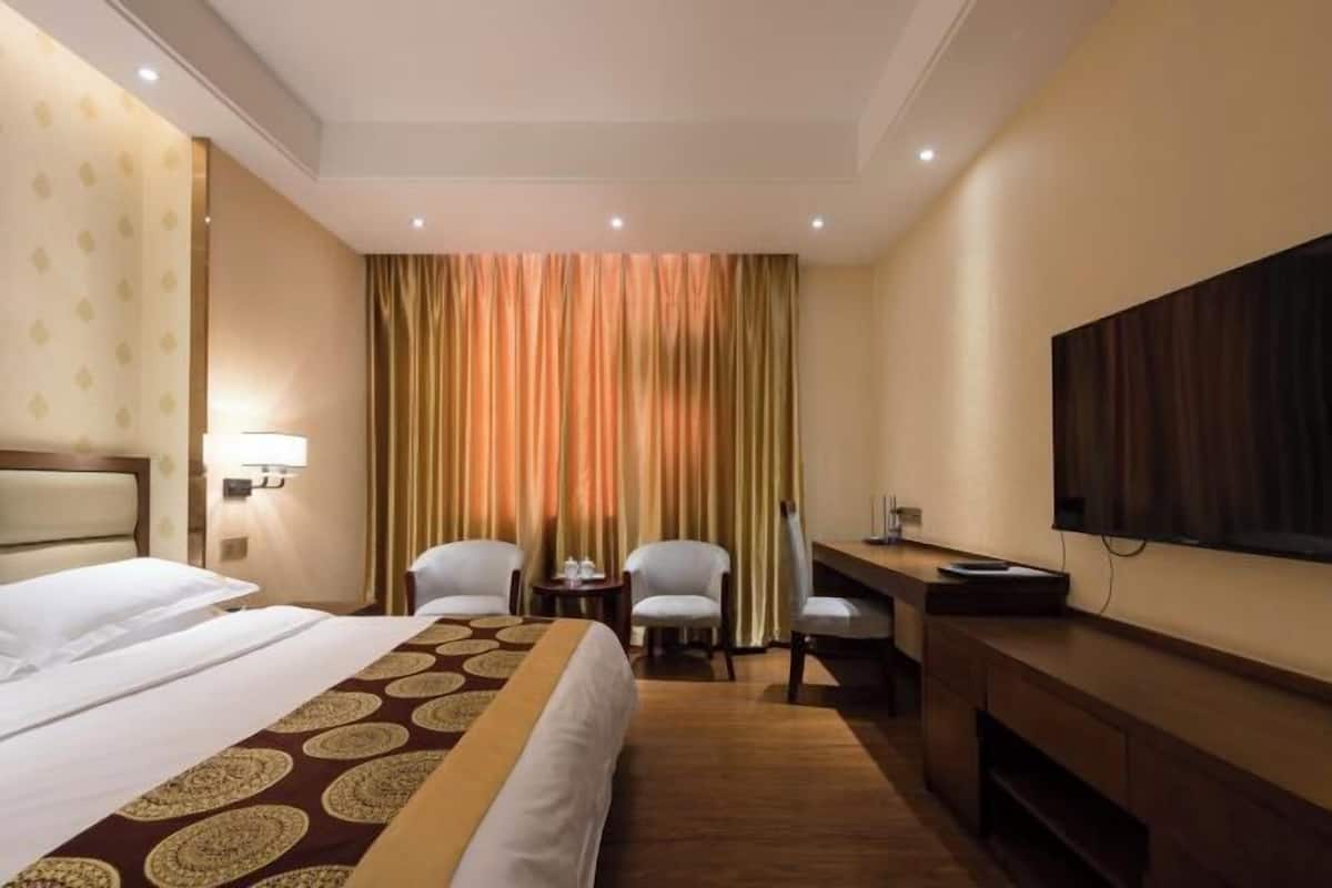 A hotel room with a bed, two chairs, a desk, a television, and a curtain.
