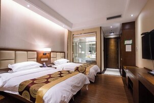 Habitación de hotel con dos camas, televisor, escritorio y baño visible a través de una puerta de cristal.