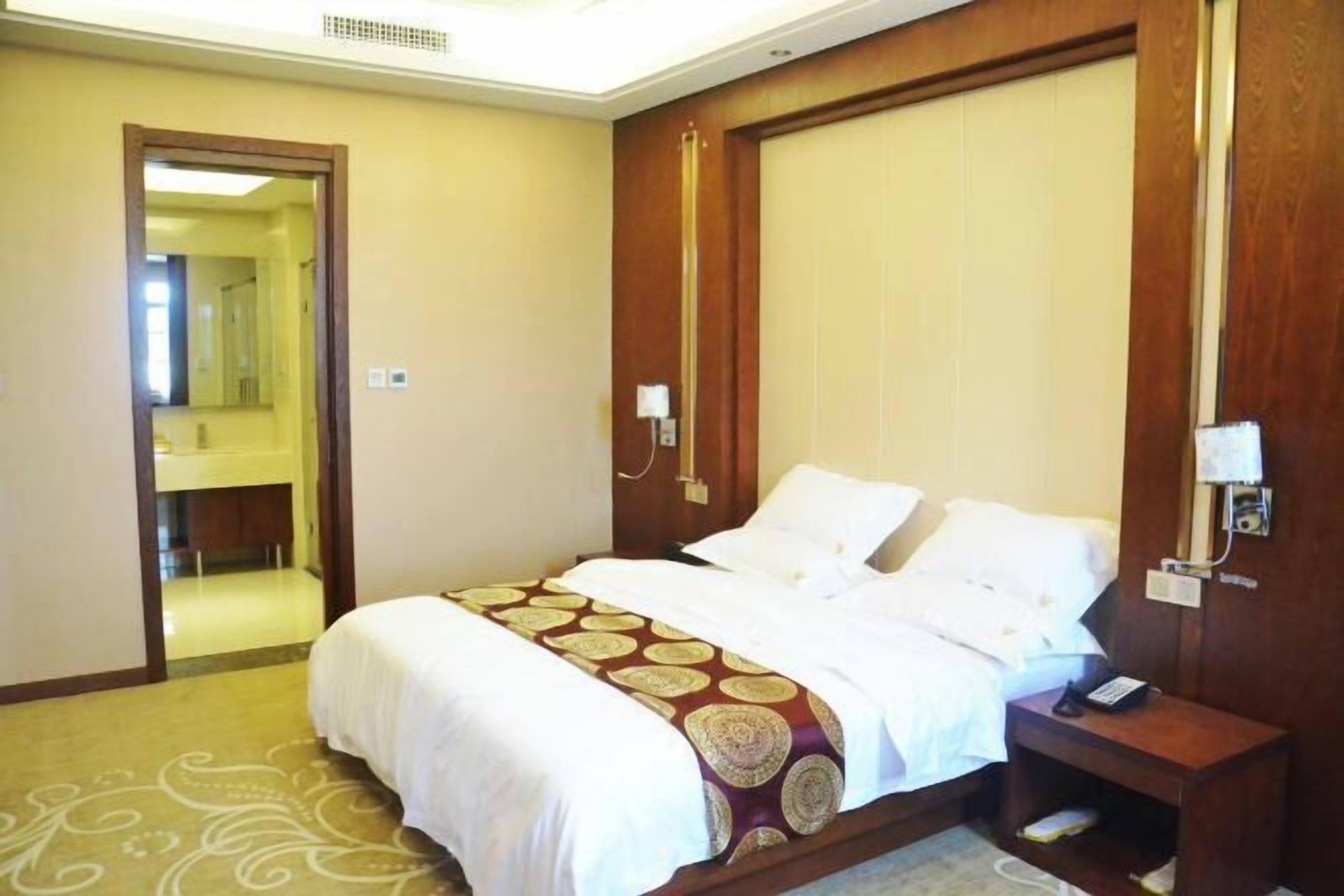 A hotel room with a large bed, a bedside table with a phone, and a mirror.