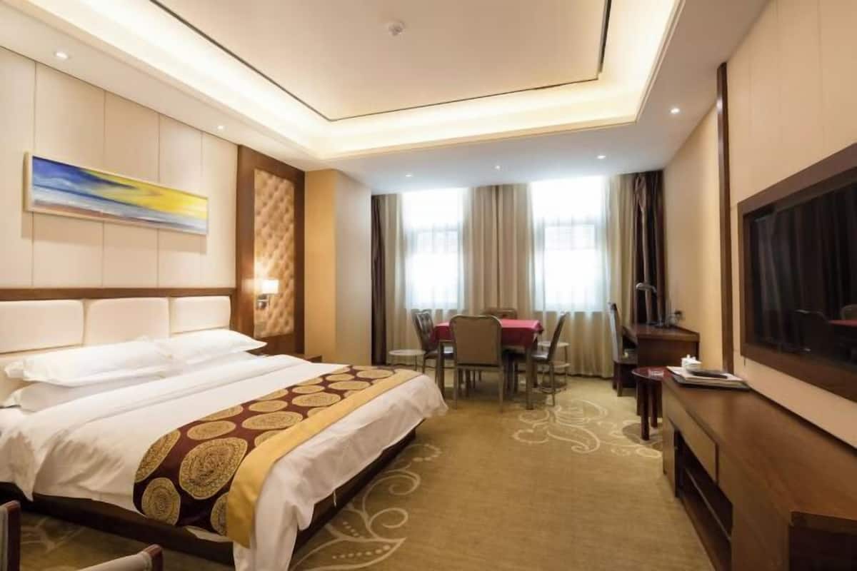 A hotel room with a large bed, a dining table, and a TV.