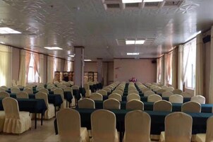 Uma sala de conferências com mesas e cadeiras dispostas em fileiras, grandes janelas e um teto decorativo.