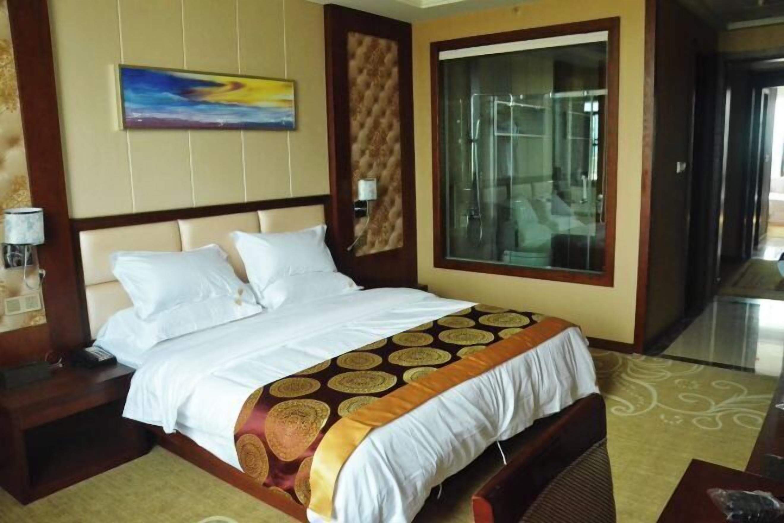 A hotel room with a large bed, a glass shower enclosure, and a painting on the wall.