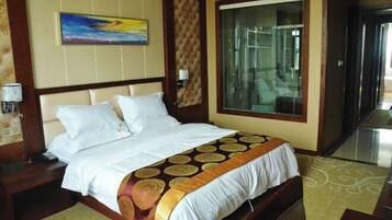 A hotel room with a large bed, a glass shower enclosure, and a painting on the wall.